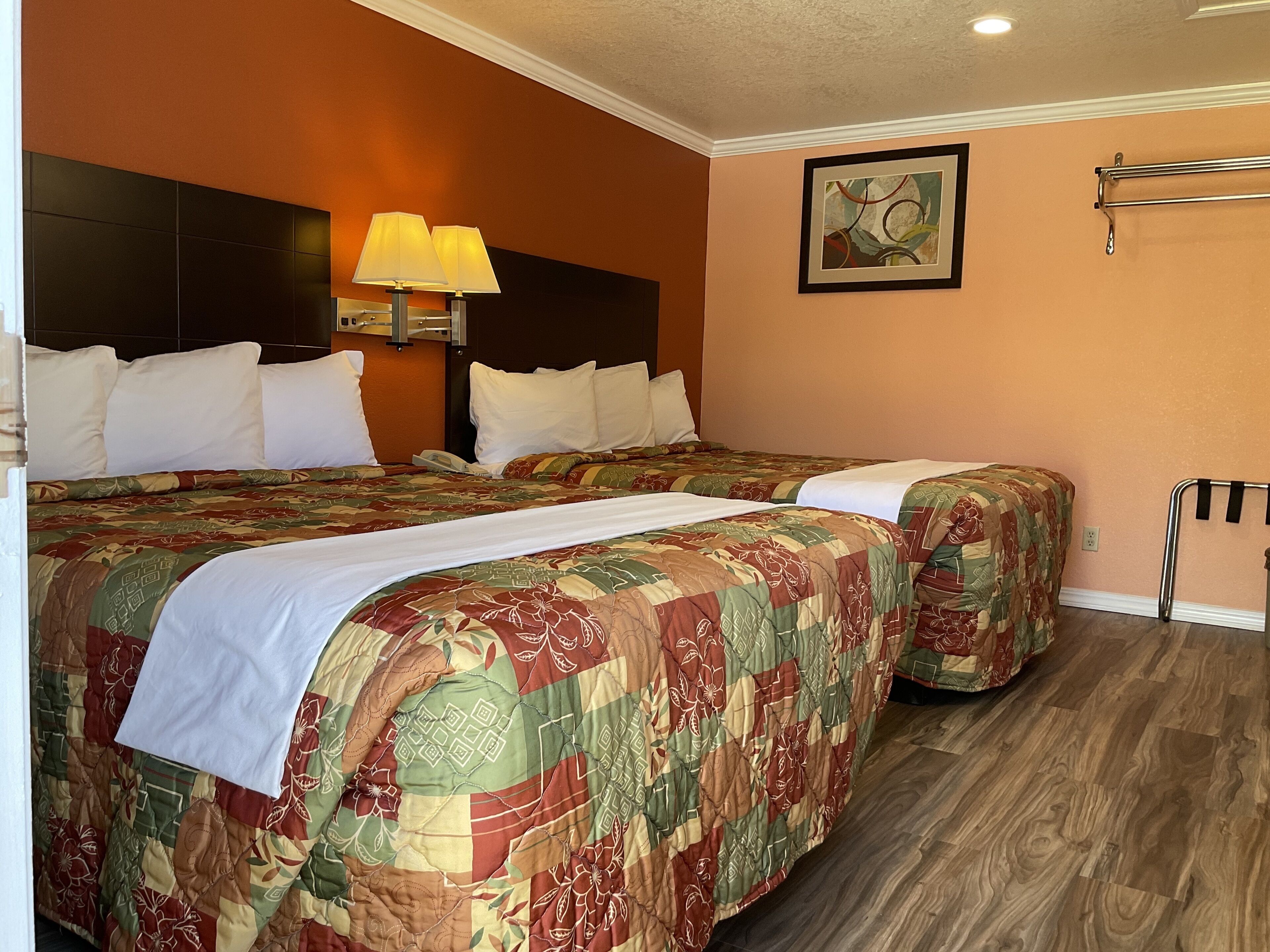 A hotel room with two beds, a nightstand, a lamp, a painting, and a towel rack.