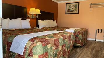 A hotel room with two beds, a nightstand, a lamp, a painting, and a towel rack.