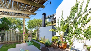 An outdoor patio with a table and chairs, surrounded by potted plants and a wooden pergola.