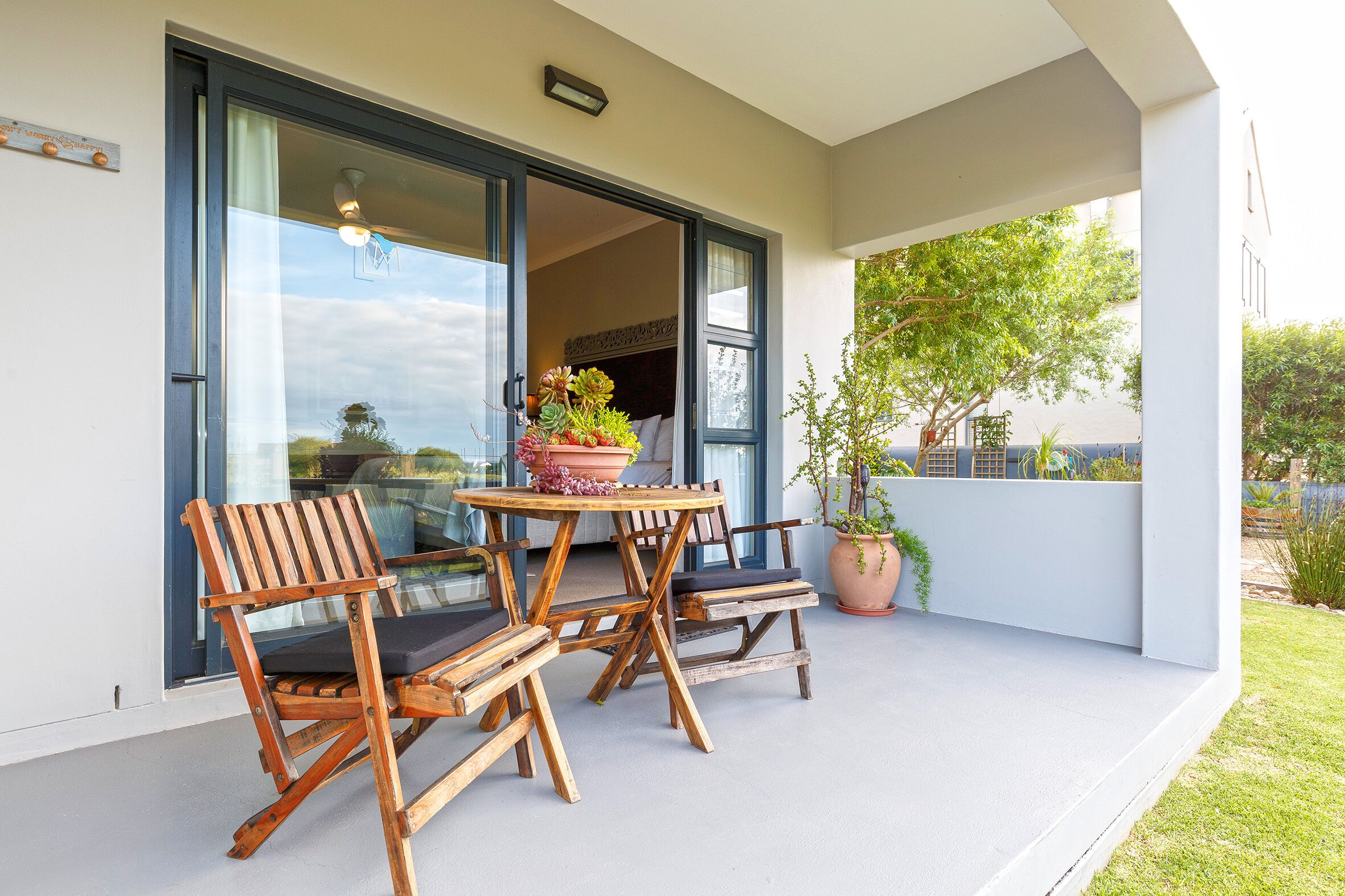 Eine Terrasse im Freien mit einem Holztisch und Stühlen, einem Blumentopf und Blick ins Innere durch eine Glastür.