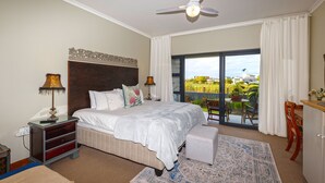 A bedroom with a large bed, a ceiling fan, a nightstand, and a view of a balcony with outdoor furniture.