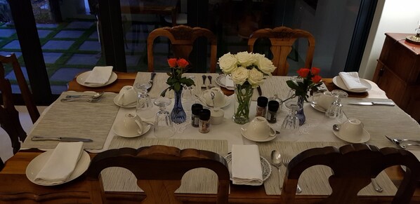 A dining table set with white plates, silverware, and glassware, surrounded by wooden chairs. - Le Mahi Guest House (Langebaan)