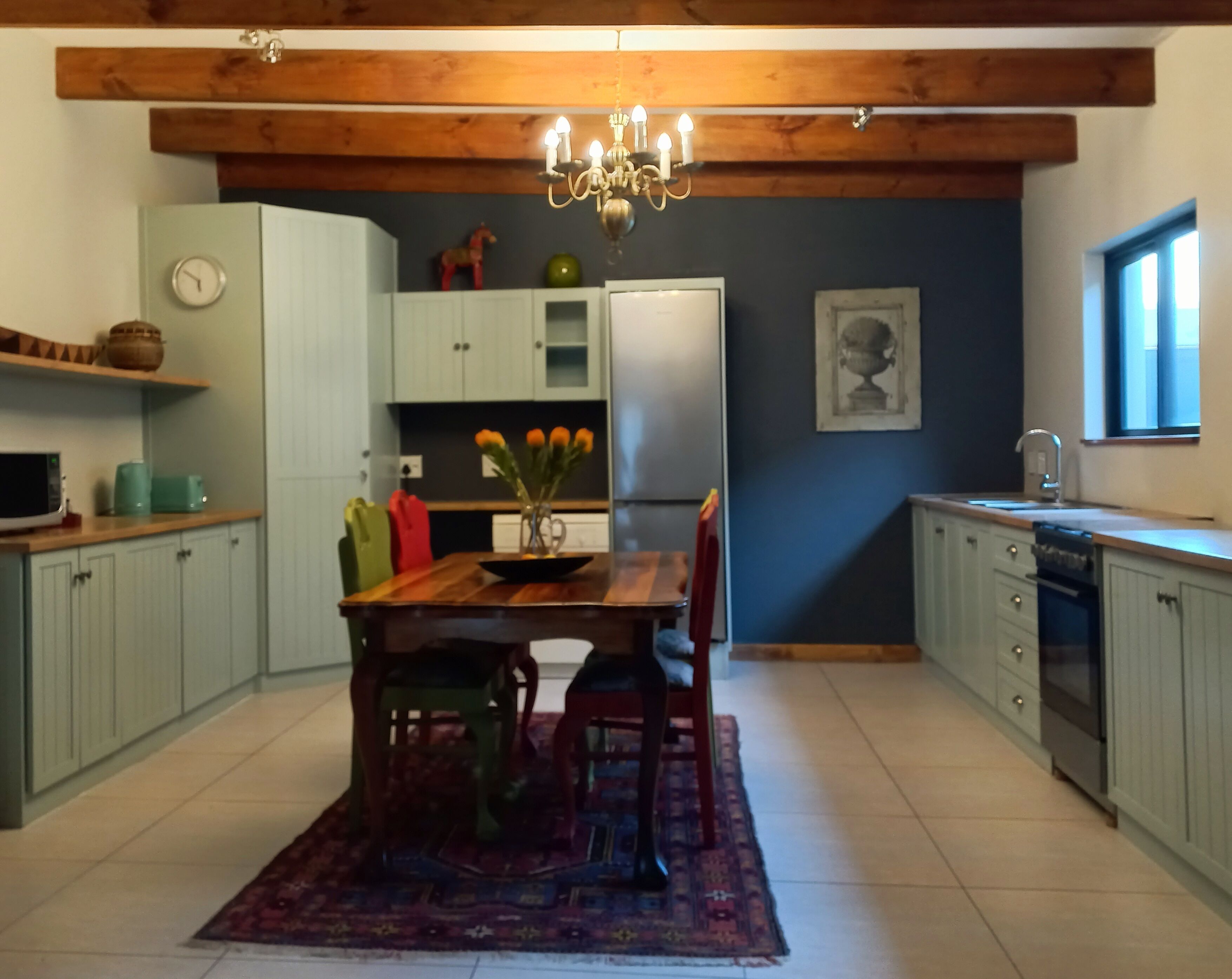 A kitchen with a wooden ceiling, a chandelier, a dining table with chairs, a refrigerator, and a window.