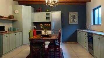 A kitchen with a wooden ceiling, a chandelier, a dining table with chairs, a refrigerator, and a window.