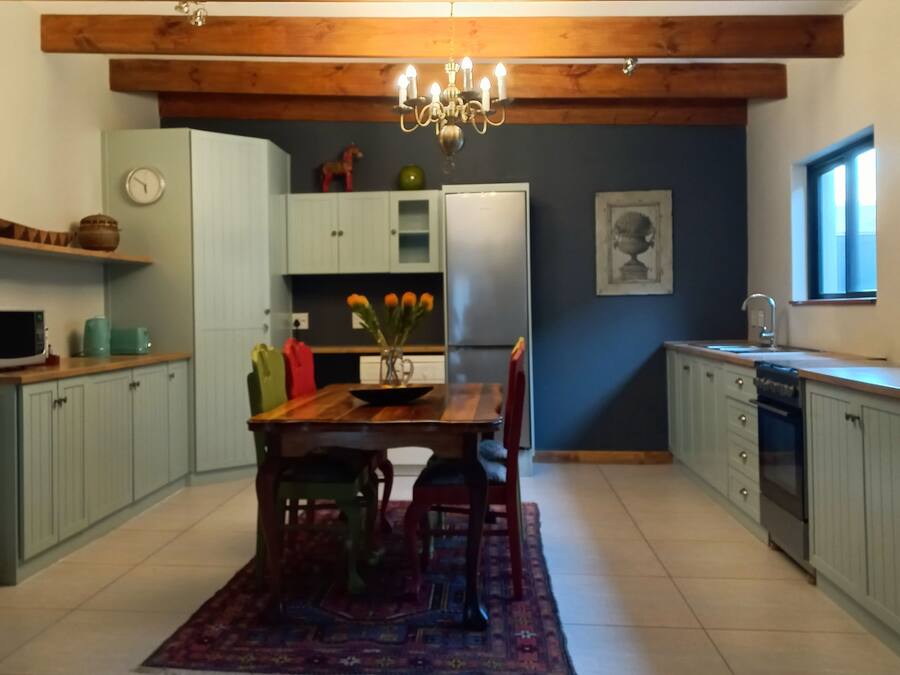 A kitchen with a wooden ceiling, a chandelier, a dining table with chairs, a refrigerator, and a window.