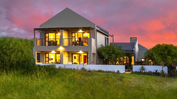A modern two-story house with a balcony, large windows, and a well-lit entrance.