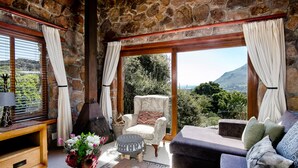 A stone-walled room with a sofa, armchair, and a table with a vase of flowers. - Leopardstone Hill (Cape Town)