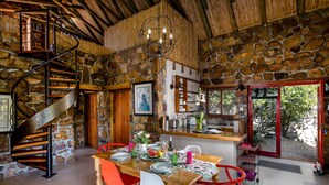 A rustic interior with a stone wall, a spiral staircase, a wooden dining table with chairs, and a kitchen area. - Leopardstone Hill (Cape Town)
