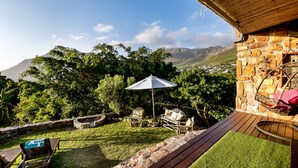 A patio with a stone wall, a wooden deck, and a view of mountains. - Leopardstone Hill (Cape Town)