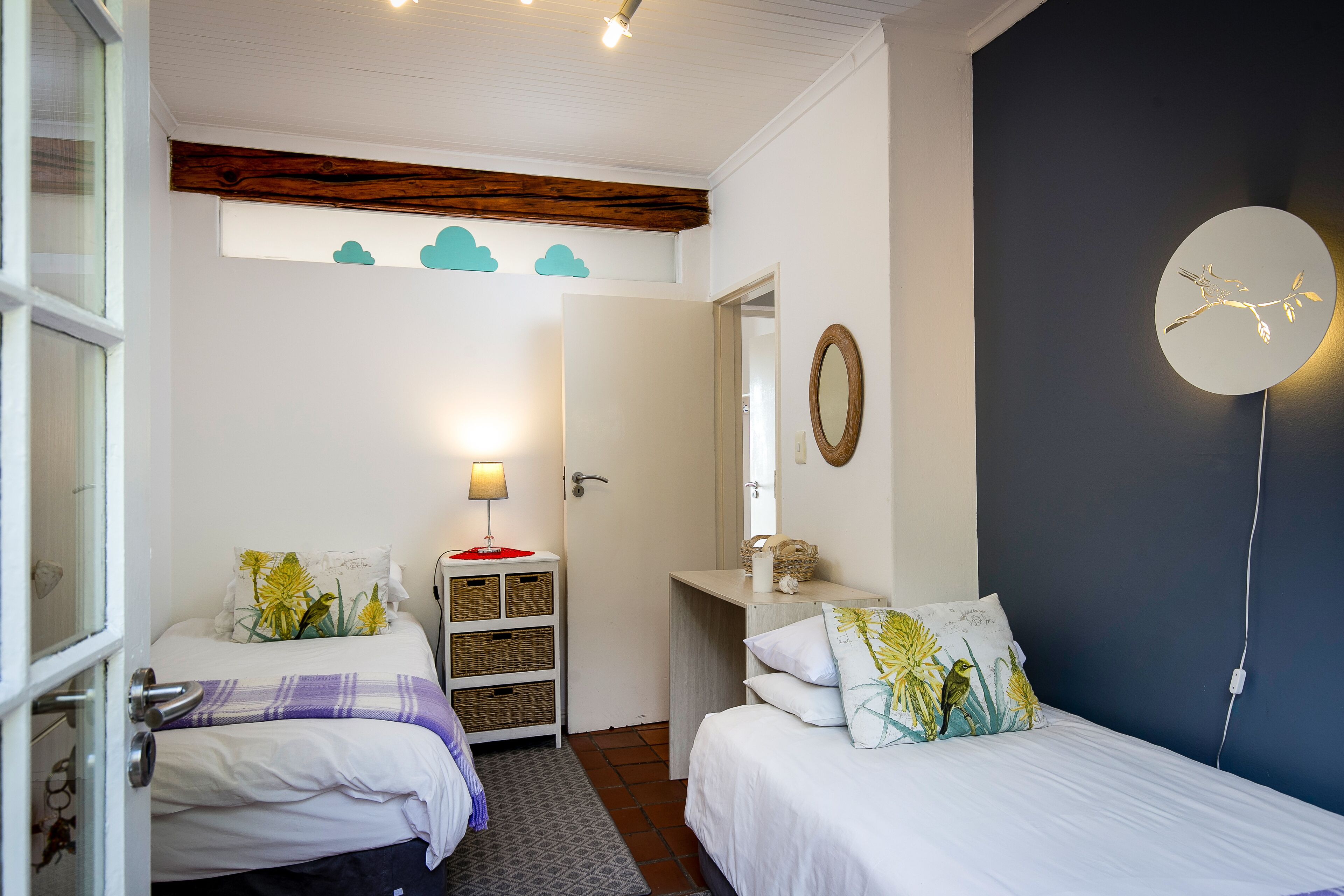 Ein Schlafzimmer mit zwei Betten, einem Holzbalken an der Decke, einem an der Wand befestigten Spiegel und einem kleinen Regal mit Körben.