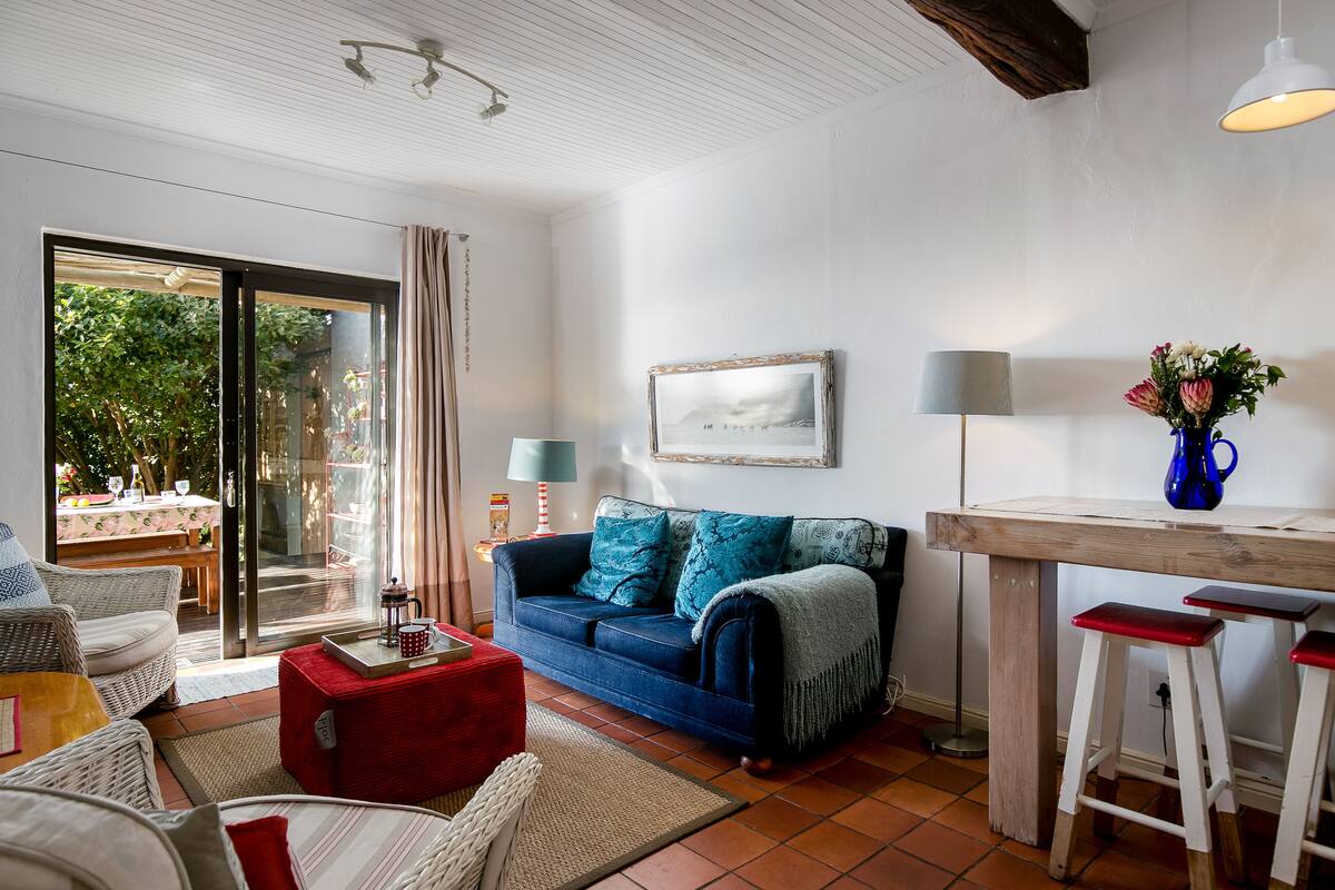 A cozy living room with a blue sofa, a red ottoman, and a wooden table with two stools.