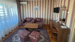 Et værelse med stribet tapet, en sofa, et lille bord, skamler, et fjernsyn og et spejl.