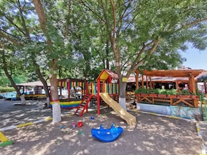 A playground with slides and climbing structures, surrounded by trees. - Olymp (Nessebar)