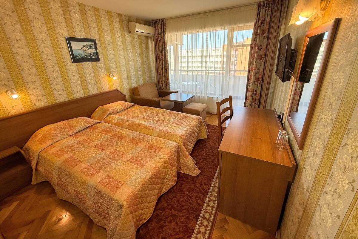 A hotel room with two beds, a desk, a chair, a TV, and a window with curtains.