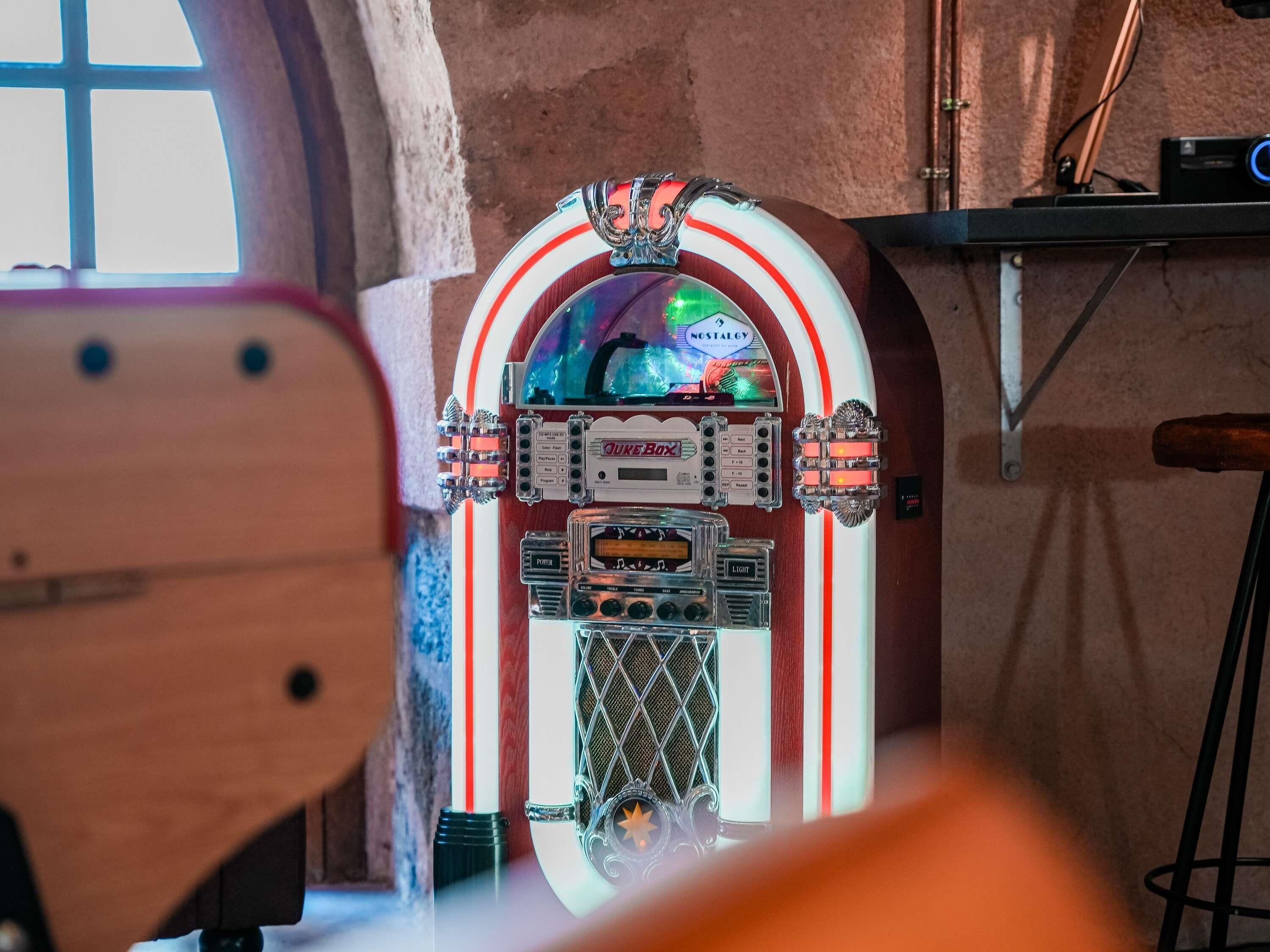 Un jukebox con diseño retro, una ventana y una repisa metálica.
