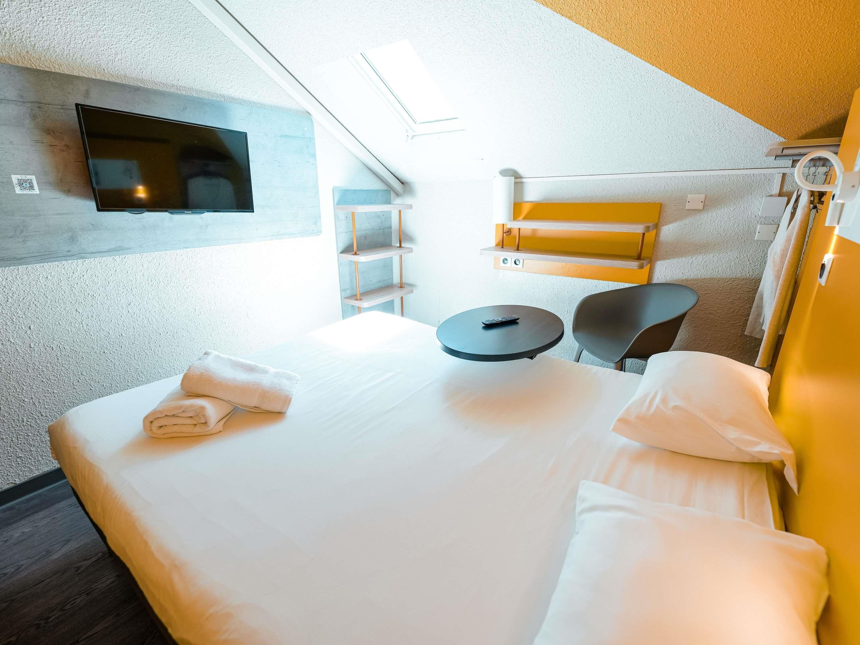 A hotel room with a bed, a TV mounted on the wall, a small round table, and a chair.