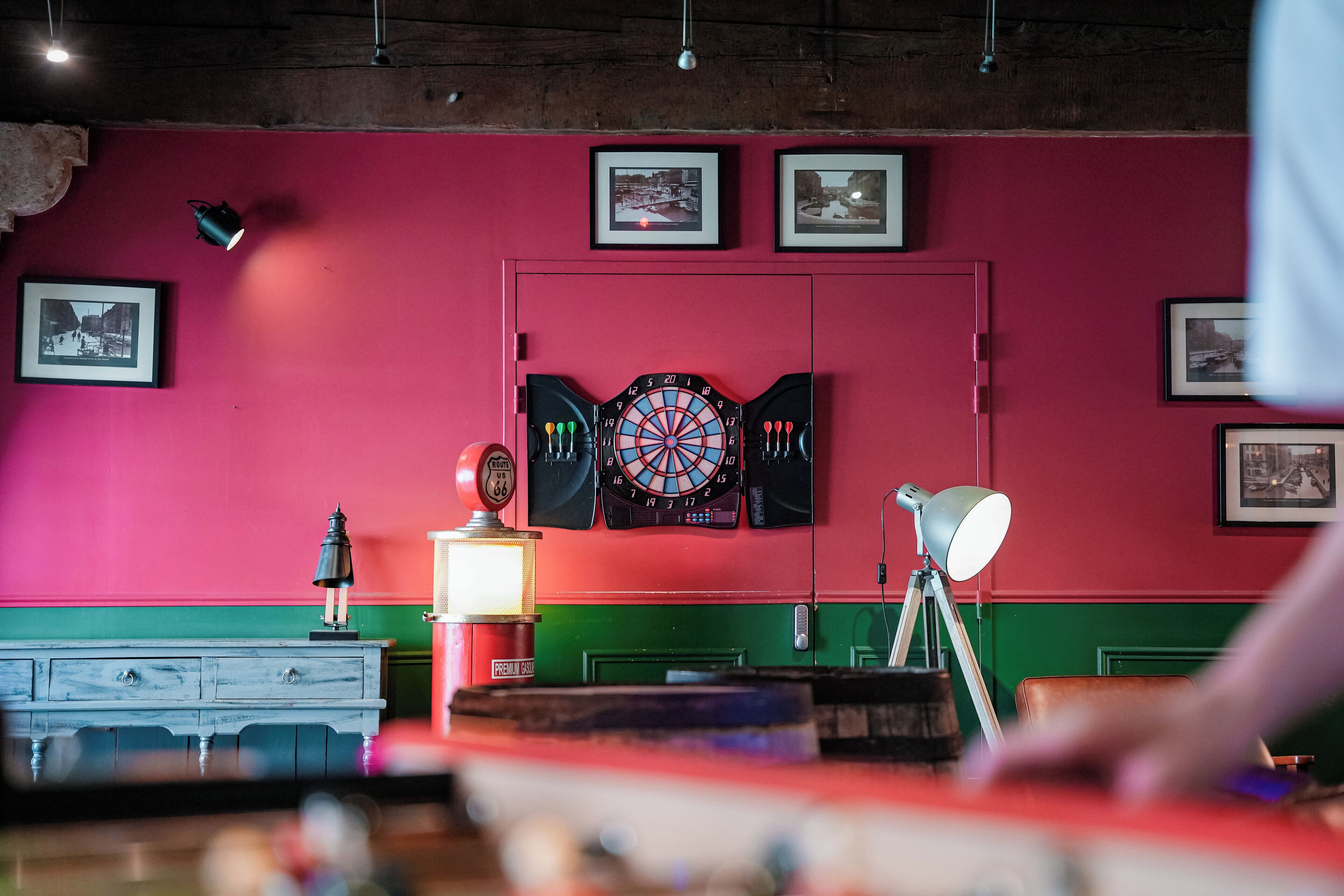 A room with a dartboard, framed pictures on the wall, and a green and red wall.