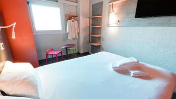 Habitación de hotel con cama, una mesita, una silla, televisión y ventana.