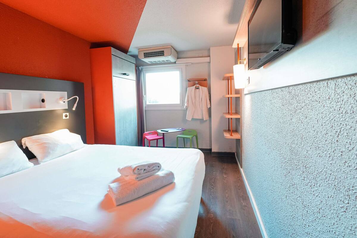 A hotel room with a bed, a desk, a chair, a TV, and a window.