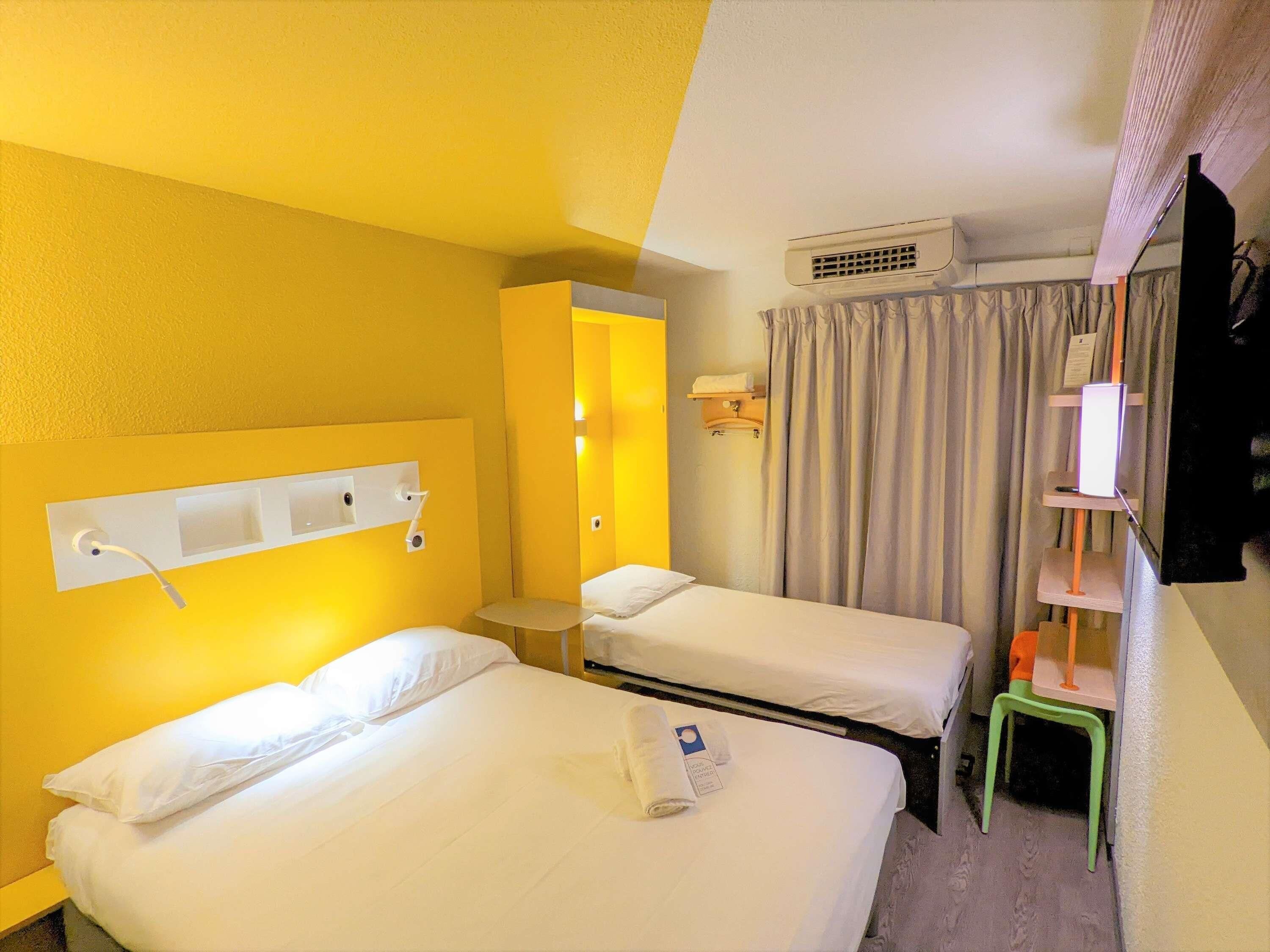 Una camera d'albergo con due letti, un piccolo tavolo, una televisione e un condizionatore.