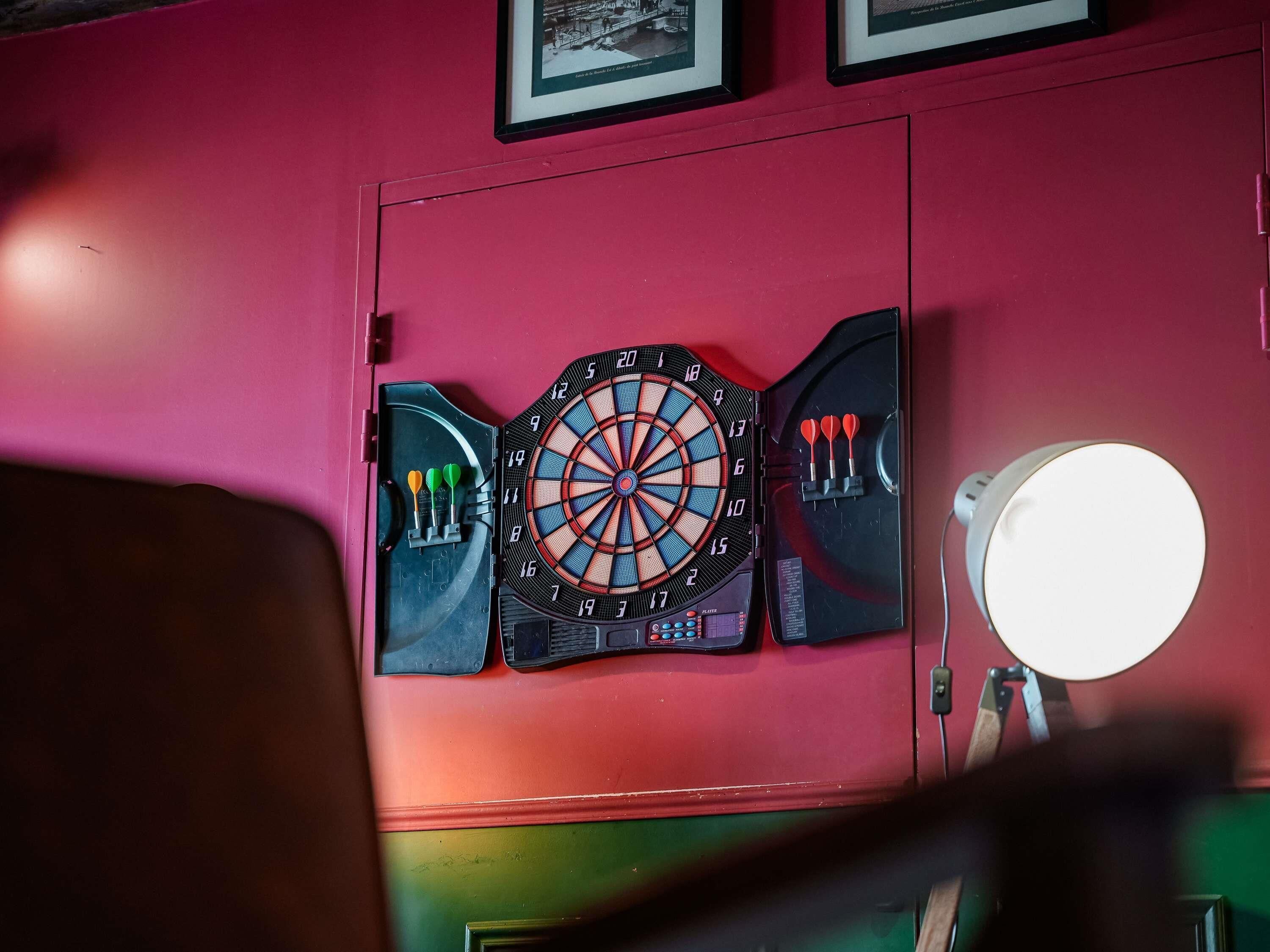 A dartboard mounted on a red wall with a dartboard case and darts beside it.
