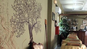 Un vestíbulo con un sillón de estampado floral, una mesa con un cubo, un mural de un árbol y una barra con mantel verde.