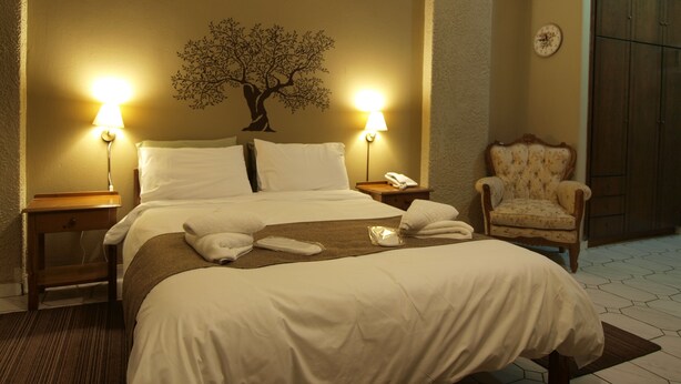 Una habitación de hotel con una cama grande, dos lámparas de noche, una silla y un reloj de pared.