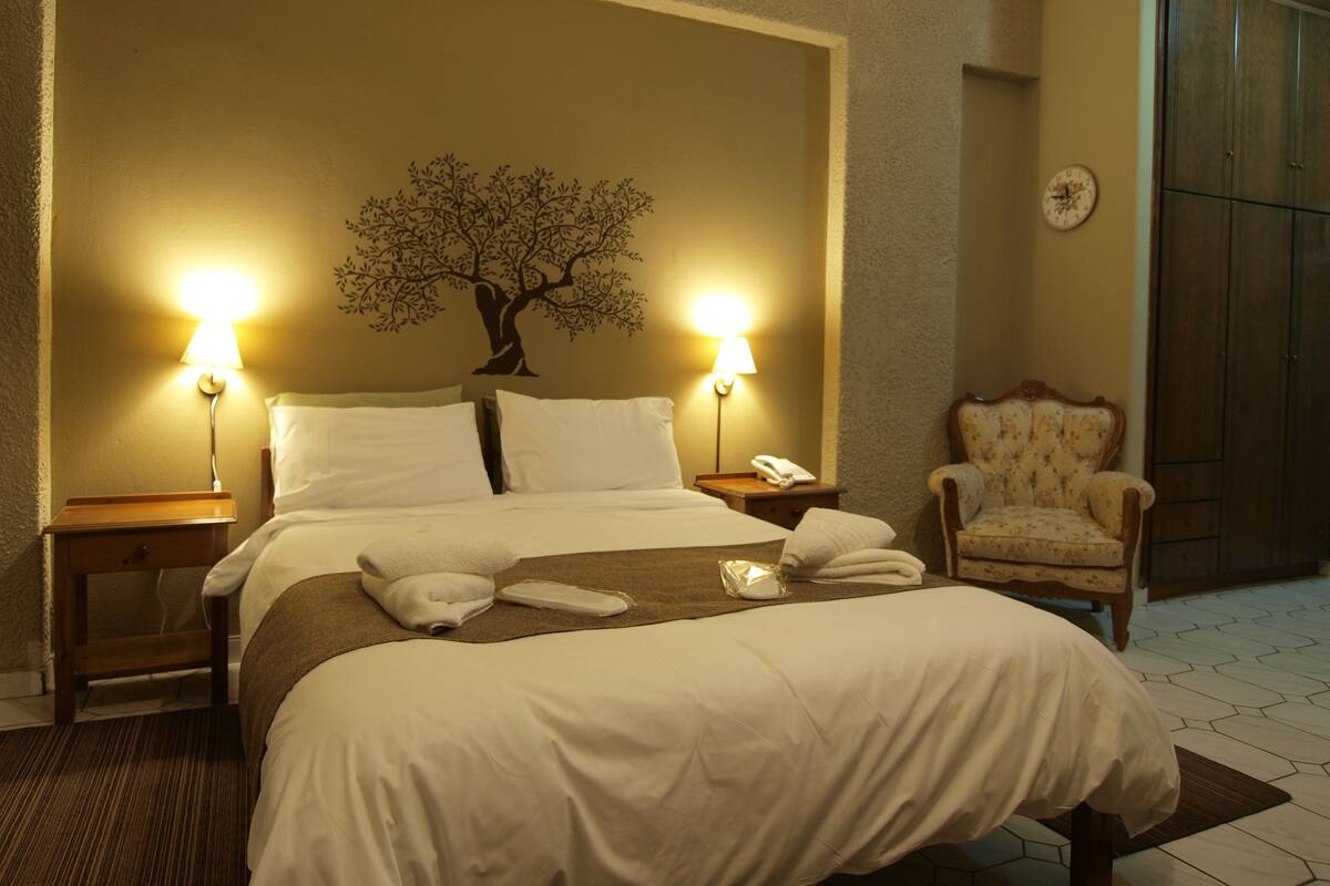 A hotel room with a large bed, two bedside lamps, a chair, and a wall clock.