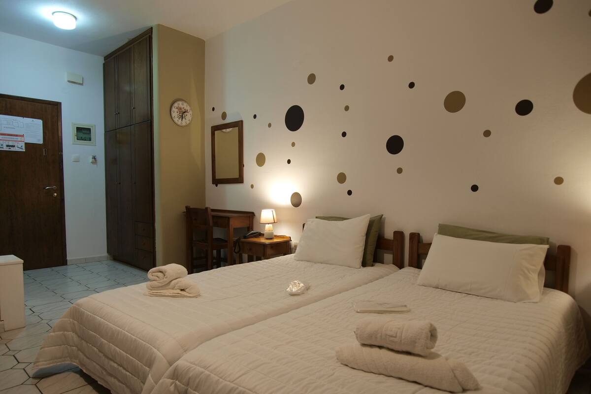 A hotel room with two beds, a desk, a chair, a clock, and a wall with circular decorations.