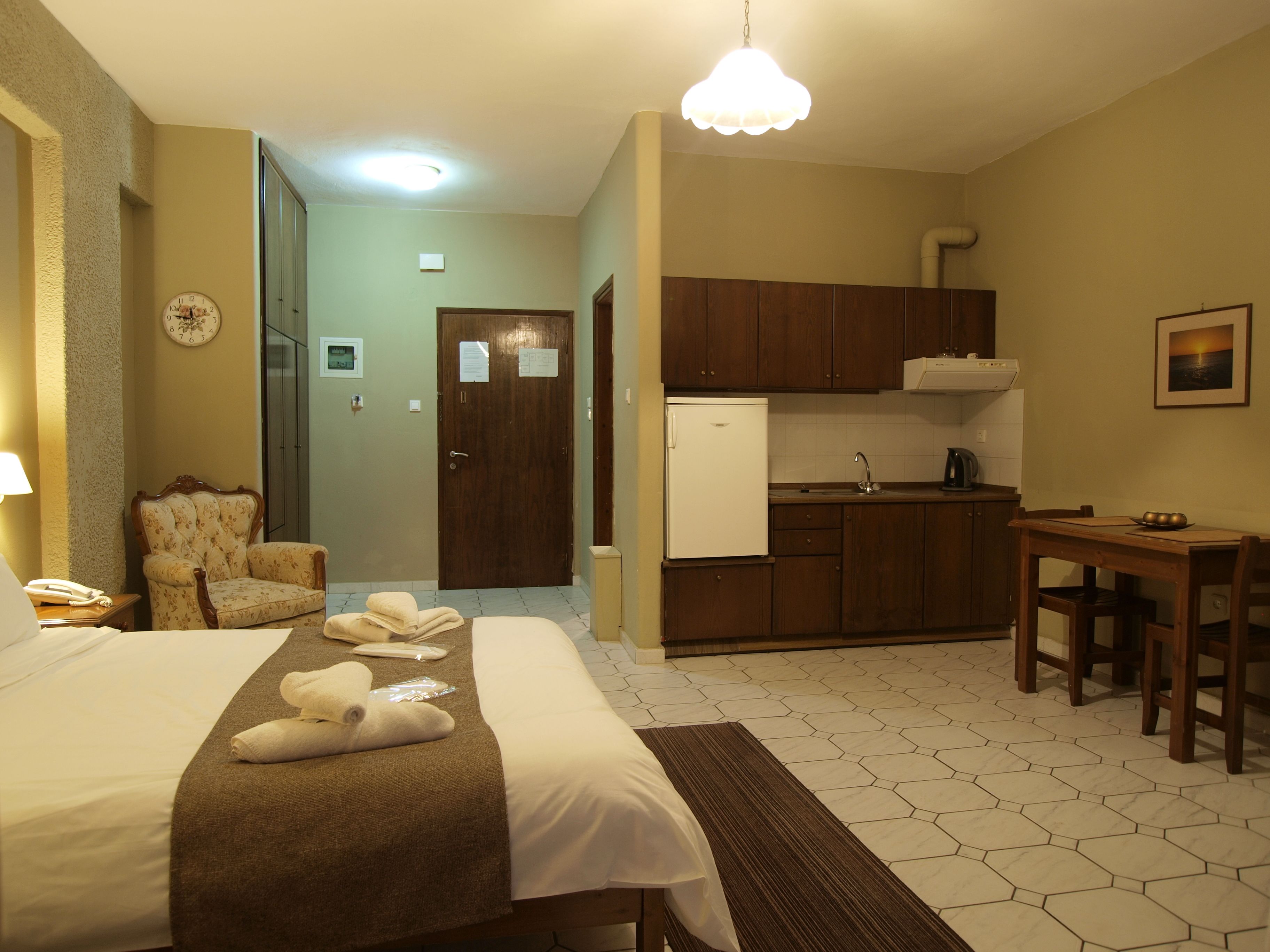 A hotel room with a bed, a chair, a small kitchen area, and a dining table.