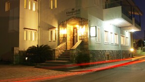 Un edificio de dos plantas con fachada de piedra, un letrero que dice "Kleopatrania Traditional Hotel - Apartments" y una escalera que lleva a la entrada.