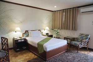 A hotel room with a wooden bed, two bedside tables with lamps, a chair, a small table, and a large window with curtains. - Oasis Hotel (Angeles City)