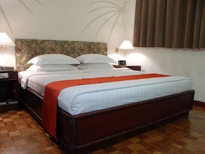 A hotel room with a large bed, wooden headboard, and a nightstand with a lamp. - Oasis Hotel (Angeles City)