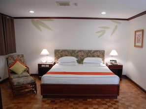 A hotel room with a large bed, two bedside tables, a chair, and a wall with leaf patterns. - Oasis Hotel (Angeles City)