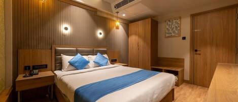 Habitación de hotel con una cama grande, cabecera de madera, mesitas de noche y un armario.