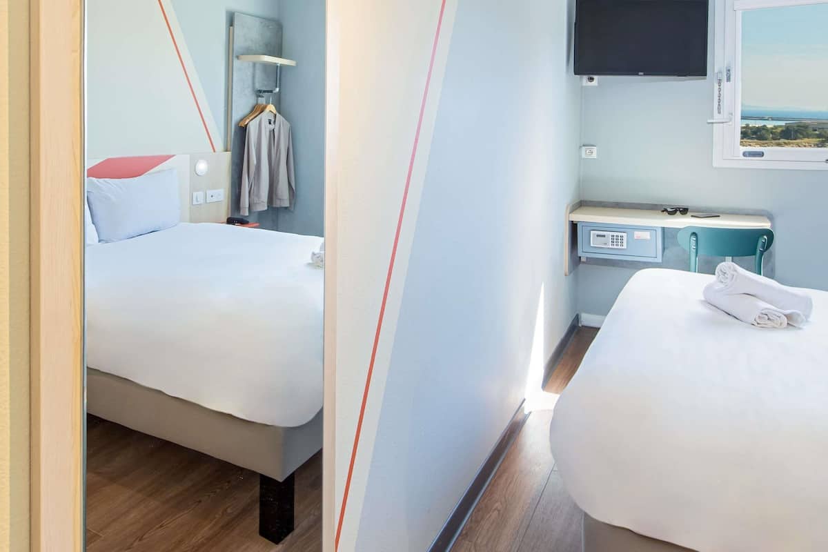 Une chambre d’hôtel avec deux lits, un bureau avec un ordinateur, une télévision et une fenêtre donnant sur un beau paysage.