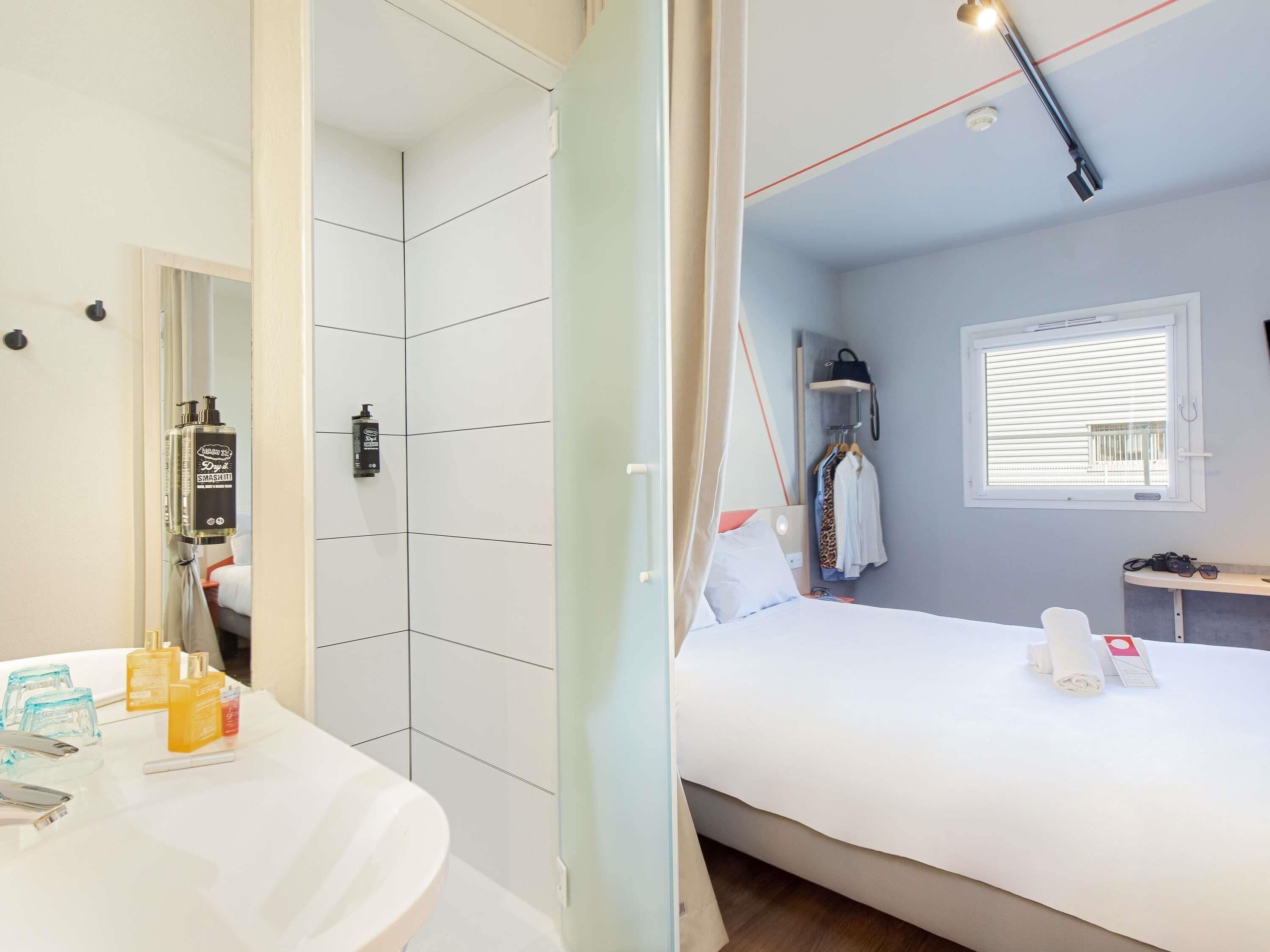 Une chambre d’hôtel avec une salle de bain, un lit, une fenêtre et un miroir.