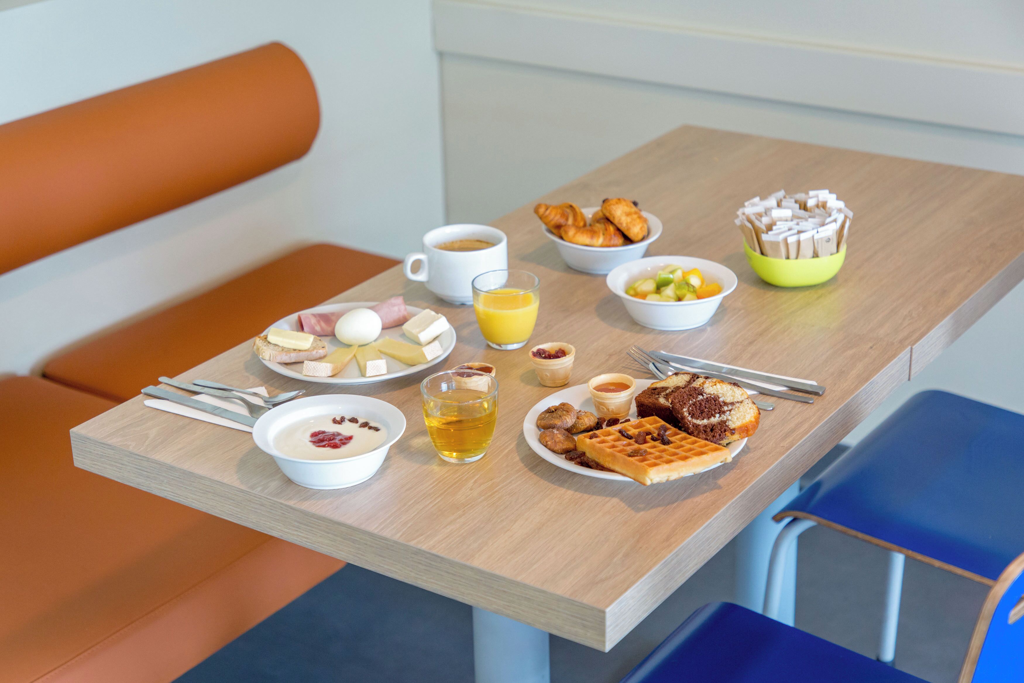 Una mesa de desayuno con diversos alimentos, una taza de café y un vaso de zumo de naranja.