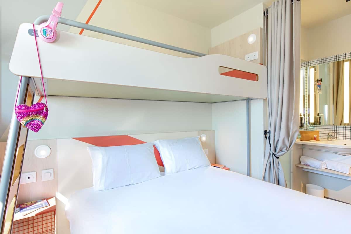 Un lit superposé avec une tête de lit, une table de chevet, un miroir et une fenêtre avec des rideaux.