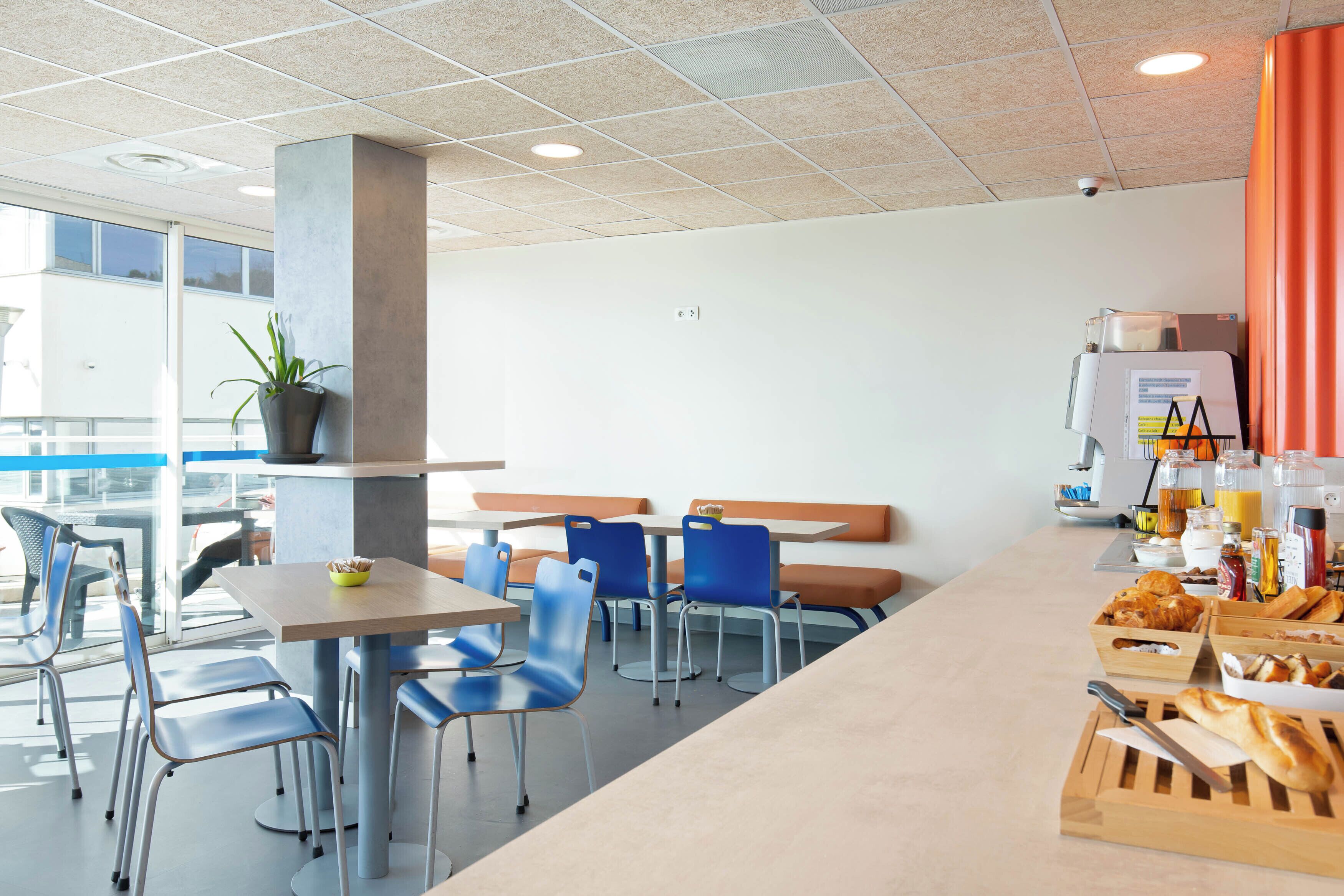 Una cafetería moderna con sillas azules, una mesa larga y diversos tipos de comida.