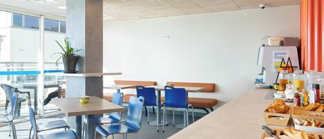 Una cafetería moderna con sillas azules, una mesa larga y diversos tipos de comida.