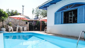A swimming pool with a stone wall and a white building with blue shutters. - World Hostel (Florianópolis)