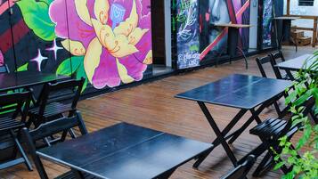An outdoor seating area with wooden tables and benches, a mural with floral and abstract designs, and a sign indicating a hostel.
