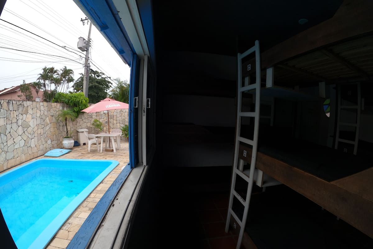 Vista di una piscina con un muro in pietra e un ombrello rosso, una scaletta in legno e un muro in pietra con una scala.