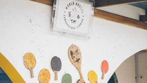 A wall with a sign reading "WORLD HOSTEL CANASUVEIRAS, FLORIPA" and a collection of uniquely designed ping pong paddles arranged in a semi-circle. - World Hostel (Florianópolis)