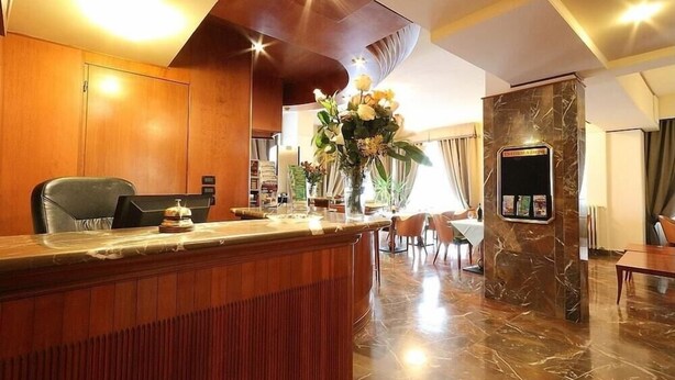 A hotel lobby with a reception desk, a marble column, and a dining area with chairs and a table. - Arcadia (Florence)