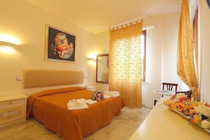 Ein Hotelzimmer mit einem großen Bett, einem kleinen Tisch mit Blumenvase, einem Spiegel und einem Gemälde an der Wand.