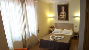 A hotel room with a bed, a desk, a chair, a painting on the wall, and a window with curtains. - Arcadia (Florence)
