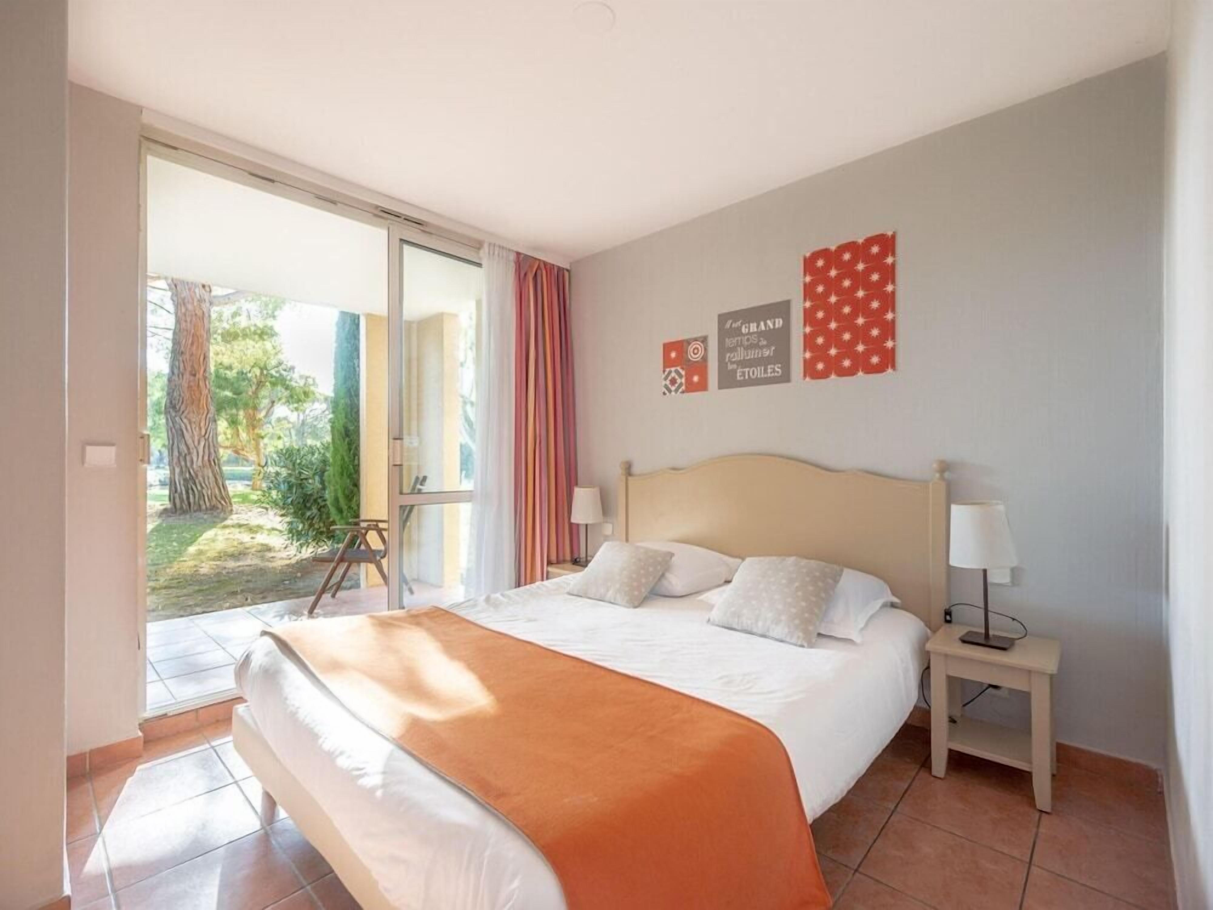 Une chambre à coucher avec un lit, une table de chevet, une lampe, une fenêtre et une vue sur l’extérieur.