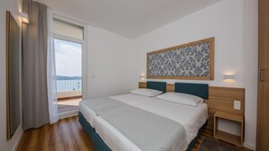 A bedroom with a large bed, a nightstand, a window with curtains, and a view of the outside. - Hotel Medena Block A (Seget)